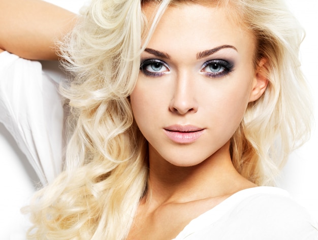 Schöne Frau mit langen blonden lockigen Haaren. Porträt des Modemodells mit hellem Make-up. Auf Weiß isoliert