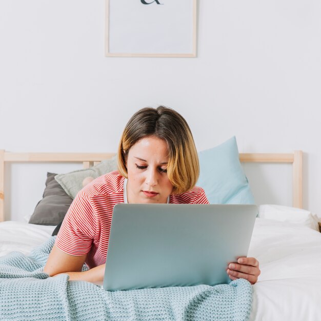 Schöne Frau mit Laptop auf dem Bett