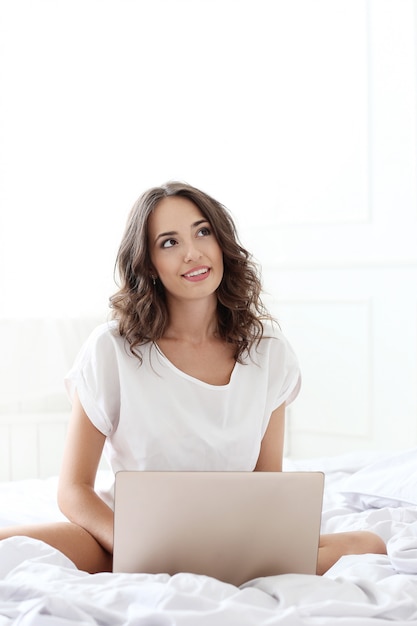 Schöne Frau mit Laptop im Bett