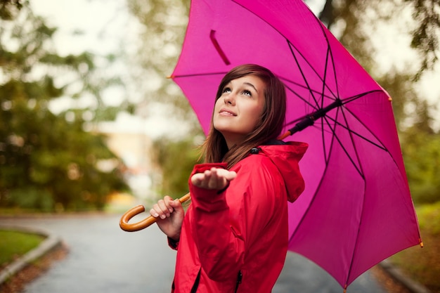 Schöne Frau mit Regenschirm, der für Regen prüft
