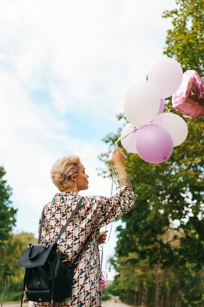 Kostenloses Foto schöne frau mit rucksack, der glücklich mit rosa luftballons im park geht. konzept für freiheit und gesunde frauen.