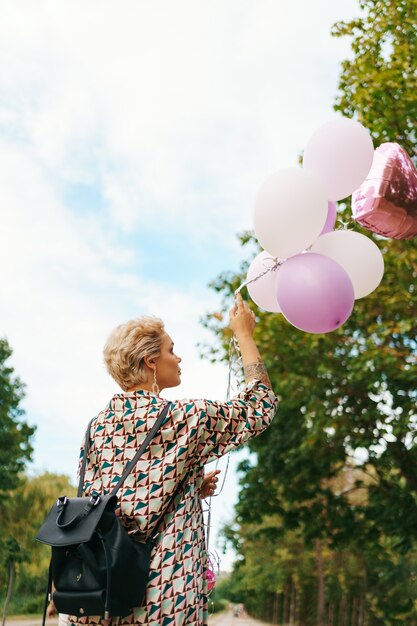 Schöne Frau mit Rucksack, der glücklich mit rosa Luftballons im Park geht. Konzept für Freiheit und gesunde Frauen.