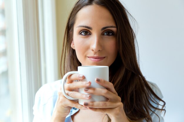 Schöne Frau trinkt Kaffee am Morgen in der Nähe des Fensters.