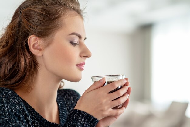Schöne Frau trinkt Kaffee und genießt den Geschmack. Hübsches junges erwachsenes Mädchen, das mit Tasse Tee entspannt.