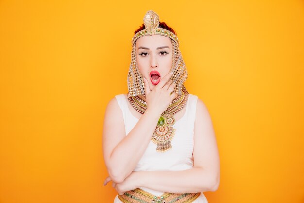 Schöne Frau wie Kleopatra im alten ägyptischen Kostüm, die auf Orange überrascht und überrascht wird