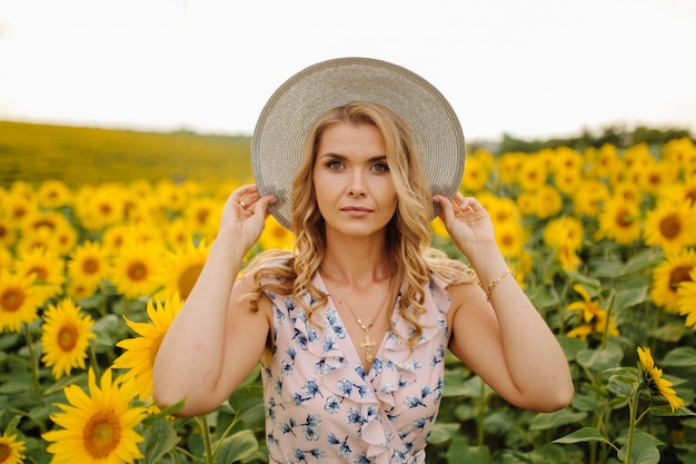 Schöne Frau wirft im landwirtschaftlichen Feld mit Sonnenblume an einem sonnigen Sommertag auf