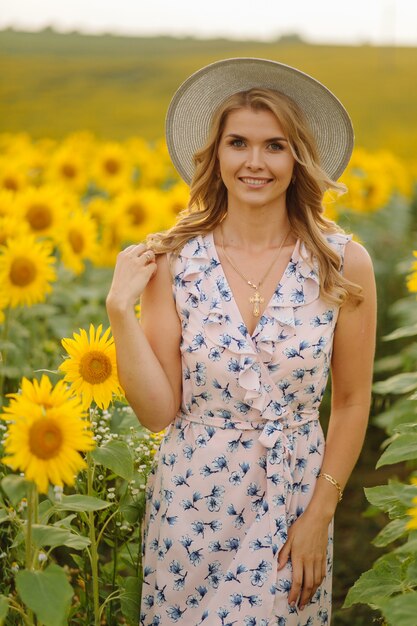 Schöne Frau wirft im landwirtschaftlichen Feld mit Sonnenblume an einem sonnigen Sommertag auf