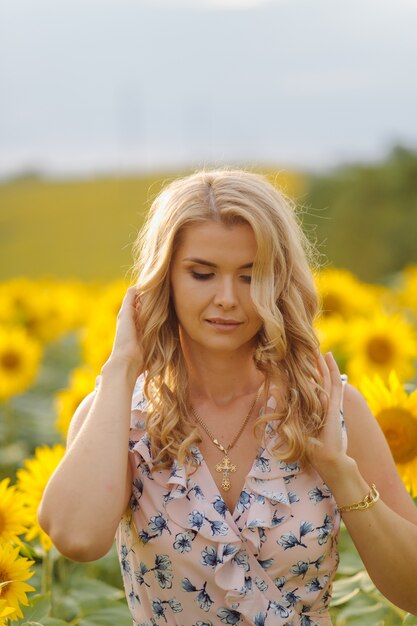 Schöne Frau wirft im landwirtschaftlichen Feld mit Sonnenblume an einem sonnigen Sommertag auf