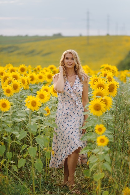 Schöne Frau wirft im landwirtschaftlichen Feld mit Sonnenblume an einem sonnigen Sommertag auf