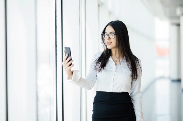 Schöne Frauen benutzen das Telefon am Panoramafenster. Geschäftskonzept