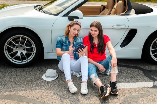 Schöne Frauen, die auf Auto sich lehnen