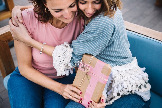 Schöne Frauen mit dem Geschenk, das auf Sofa umarmt