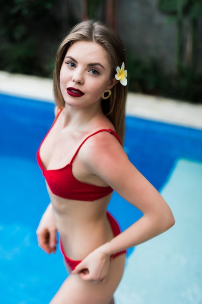 Schöne gebräunte Frau mit perfektem Körper und Haaren im Bikini, die im sonnigen Schwimmbad aufwerfen. Sinnliches junges Mädchen, das sich entspannt und Urlaub auf Luxusvilla genießt.