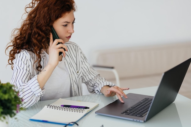 Schöne Geschäftsfrau, die an Projekten arbeitet Junge Geschäftsfrau, die mit dem Telefon am Schreibtisch spricht