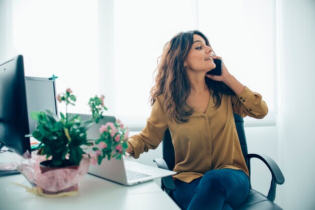 Schöne Geschäftsfrau mit ihrem Laptop und spricht am Telefon