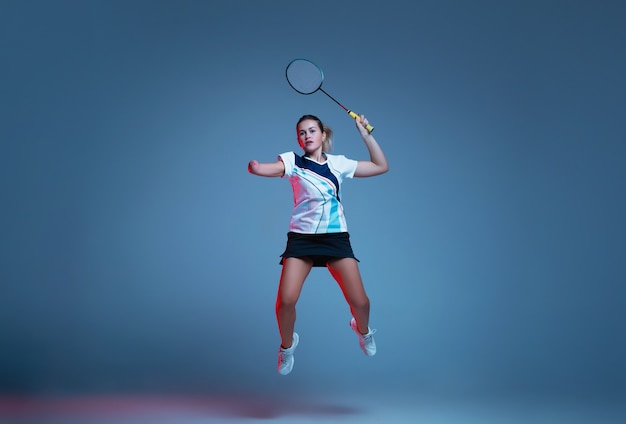 Schöne Handicapfrau, die im Badminton lokalisiert auf blauem Hintergrund im Neonlicht übt. Lebensstil integrativer Menschen, Vielfalt und Gleichheit. Sport, Aktivität und Bewegung. Copyspace für Anzeige.