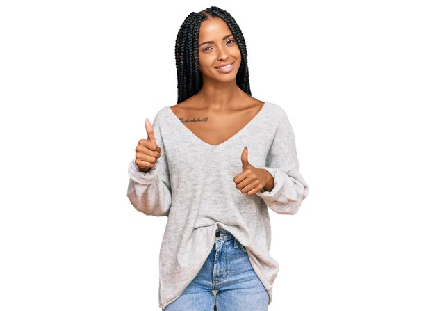 Schöne hispanische Frau trägt legere Kleidung und macht eine positive Geste mit der Hand, den Daumen hoch, lächelnd und glücklich. Fröhlicher Gesichtsausdruck und Siegergeste.