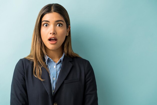 Schöne hispanische Geschäftsfrau, die im Studio mit offenem Mund unter Schock steht