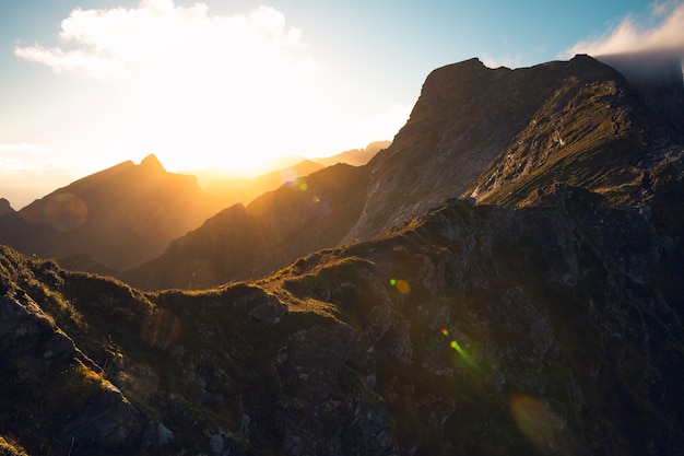 Schöne horizontale Aufnahme der aufgehenden Sonne und der hohen felsigen Berge unter dem bewölkten Himmel