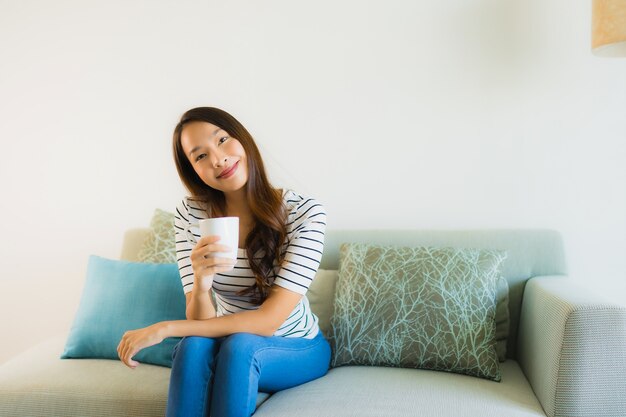 Schöne junge asiatische Frau des Porträts auf Sofa mit Kaffeetasse