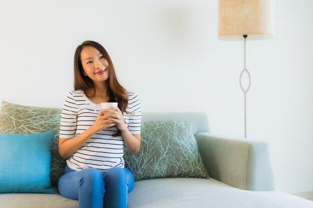 Schöne junge asiatische Frau des Porträts auf Sofa mit Kaffeetasse
