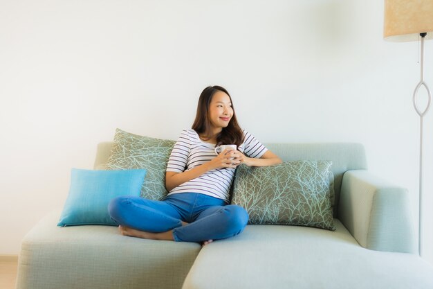 Schöne junge asiatische Frau des Porträts auf Sofa mit Kaffeetasse