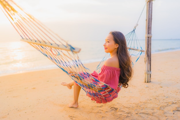 Schöne junge asiatische frau des porträts, die auf der hängematte mit glücklichem neary strandmeer und -oce des lächelns sitzt