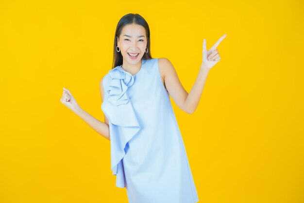Schöne junge asiatische Frau des Porträts, die auf Gelb lächelt