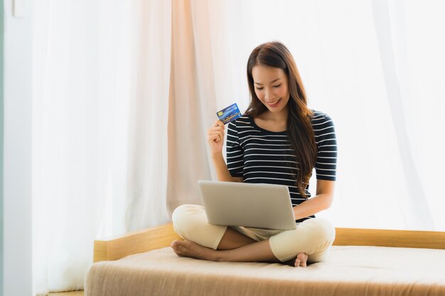 Schöne junge asiatische Frau des Porträts, die Computernotizbuch oder Laptop mit Kreditkarte für den Einkauf verwendet