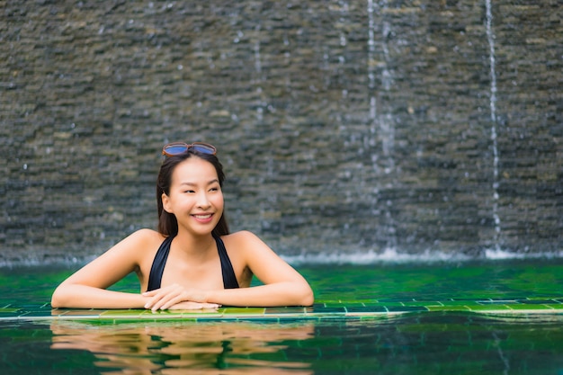 Schöne junge asiatische frau des porträts im swimmingpool um hotel und erholungsort