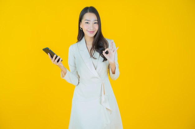 Schöne junge asiatische Frau des Porträts lächeln mit intelligentem Handy auf Farbhintergrund