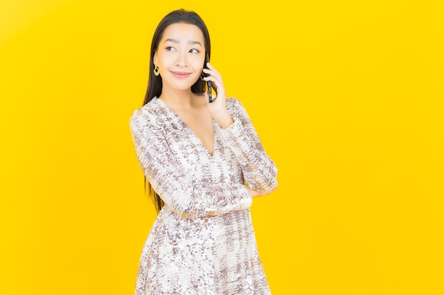 Schöne junge asiatische Frau des Porträts lächeln mit intelligentem Handy auf Gelb