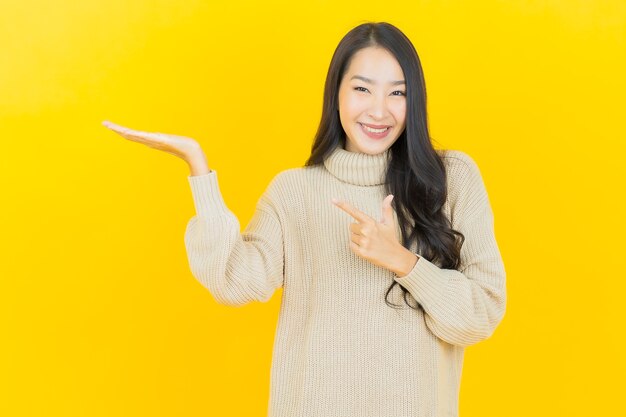 Schöne junge asiatische Frau des Porträts lächelt mit Aktion auf gelber Wand