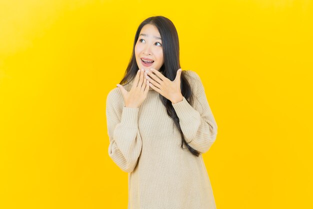 Schöne junge asiatische Frau des Porträts lächelt mit Aktion auf gelber Wand