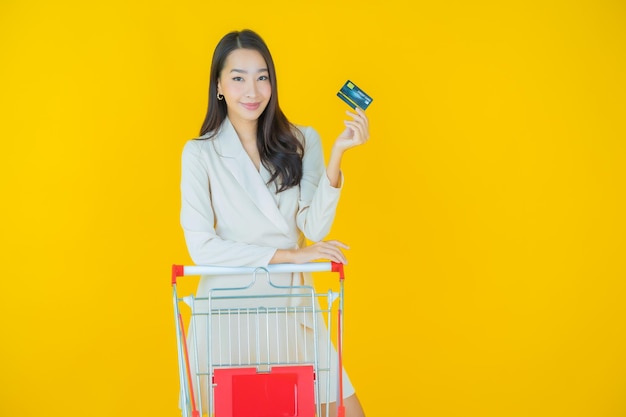 Schöne junge asiatische frau des porträts lächelt mit einkaufskorb aus dem supermarkt auf farbigem hintergrund