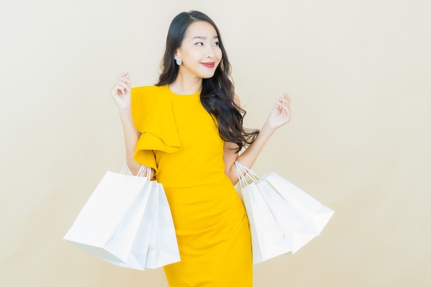 Schöne junge asiatische Frau des Porträts lächelt mit Einkaufstasche auf beige Wand