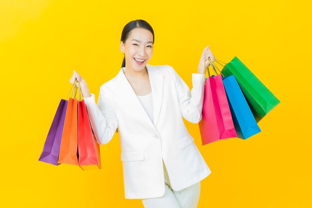 Schöne junge asiatische Frau des Porträts lächelt mit Einkaufstüten auf Farbwand