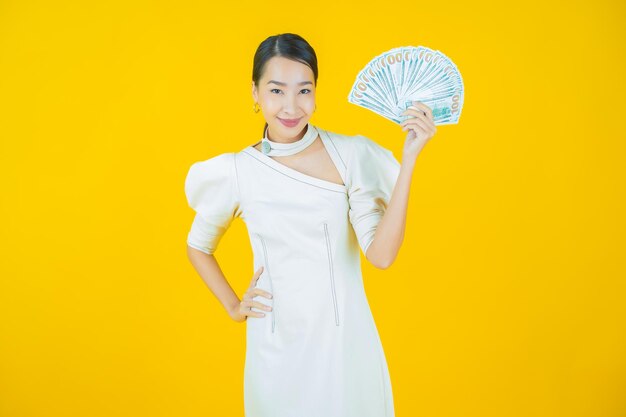 Schöne junge asiatische Frau des Porträts lächelt mit viel Bargeld und Geld auf Farbhintergrund