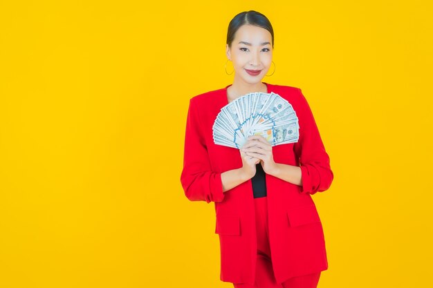 Schöne junge asiatische Frau des Porträts lächelt mit viel Bargeld und Geld auf Gelb