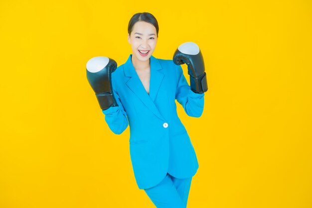 Schöne junge asiatische Frau des Porträts mit Boxhandschuh auf Gelb