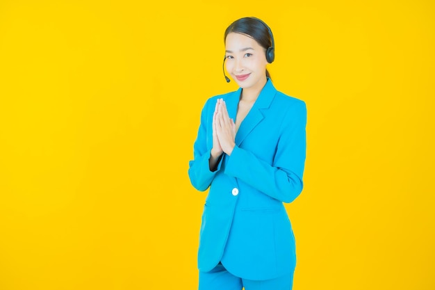Schöne junge asiatische Frau des Porträts mit Callcenter-Kundenbetreuungszentrum auf Gelb