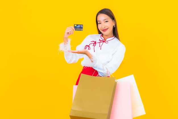 Schöne junge asiatische frau des porträts mit einkaufstasche und kreditkarte auf gelb