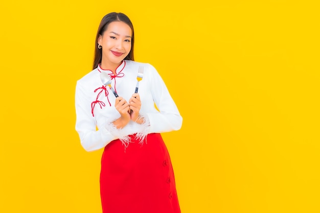 Schöne junge asiatische frau des porträts mit löffel und gabel auf gelb