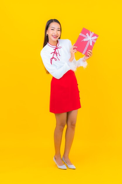 Schöne junge asiatische Frau des Porträts mit roter Geschenkbox auf Gelb