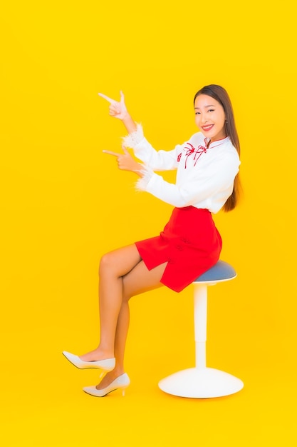 Schöne junge asiatische Frau des Porträts sitzen auf Stuhl auf Gelb
