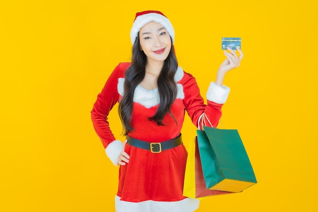 Schöne junge asiatische Frau des Porträts trägt Weihnachtskostüm mit Einkaufstasche auf Gelb