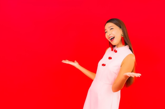 Schöne junge asiatische Frau des Porträts tragen chinesische Kleidung des neuen Jahres auf roter Wand