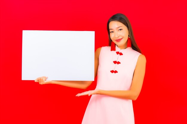 Schöne junge asiatische Frau des Porträts zeigen weiße leere Anschlagtafel auf roter Wand