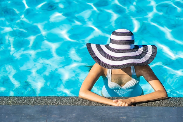 Schöne junge asiatische frau mit hut im swimmingpool für reise und ferien