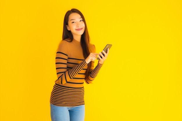 Schöne junge asiatische Frau verwenden intelligentes Handy oder Handy mit vielen Aktionen auf gelbem Hintergrund